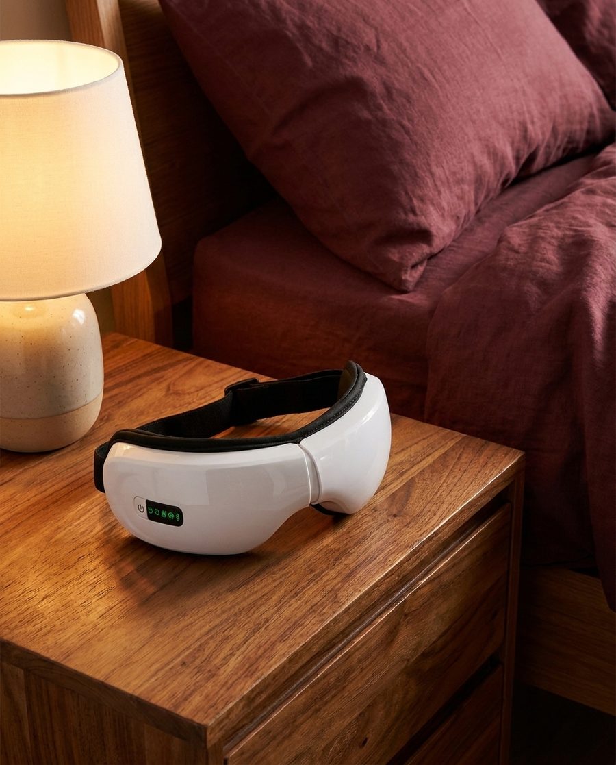 The Duvela massager resting on a warm nightstand beside a lamp.